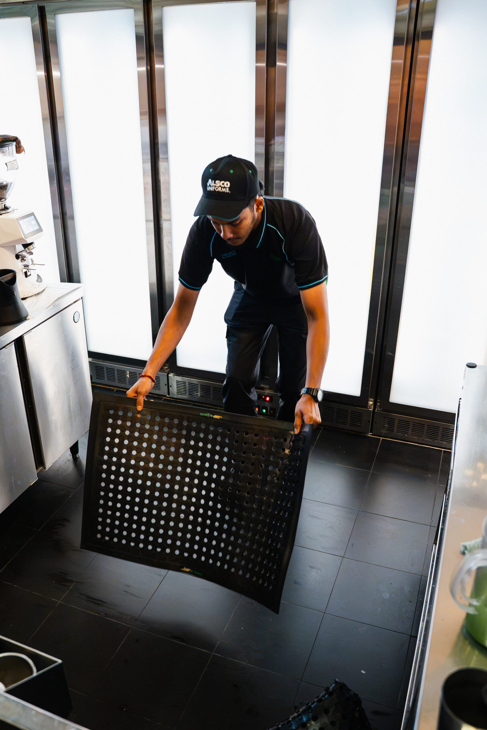 Alsco team member installing a premium anti-slip floor mat in a cafe